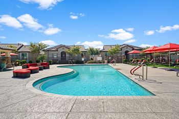 A swimming pool with red chairs and umbrellas and apartments in the background